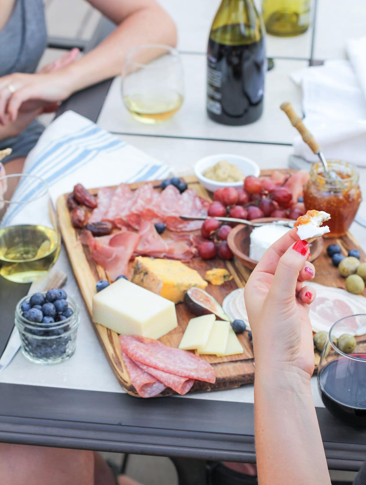 Two women making cheese and crackers out of a charcuterie board with glasses of wine.