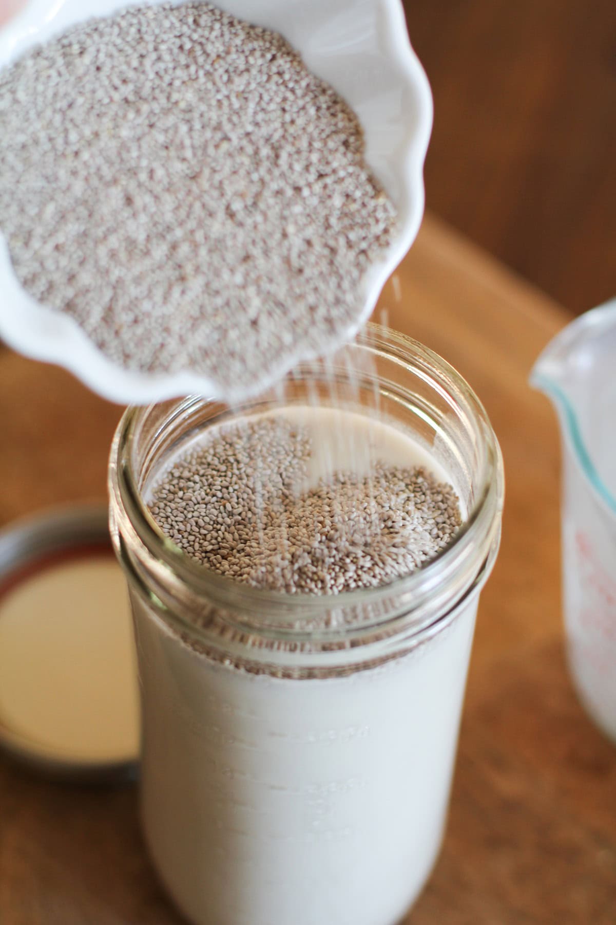 Pouring chia seeds into a jar with almond milk to make chia seed pudding.