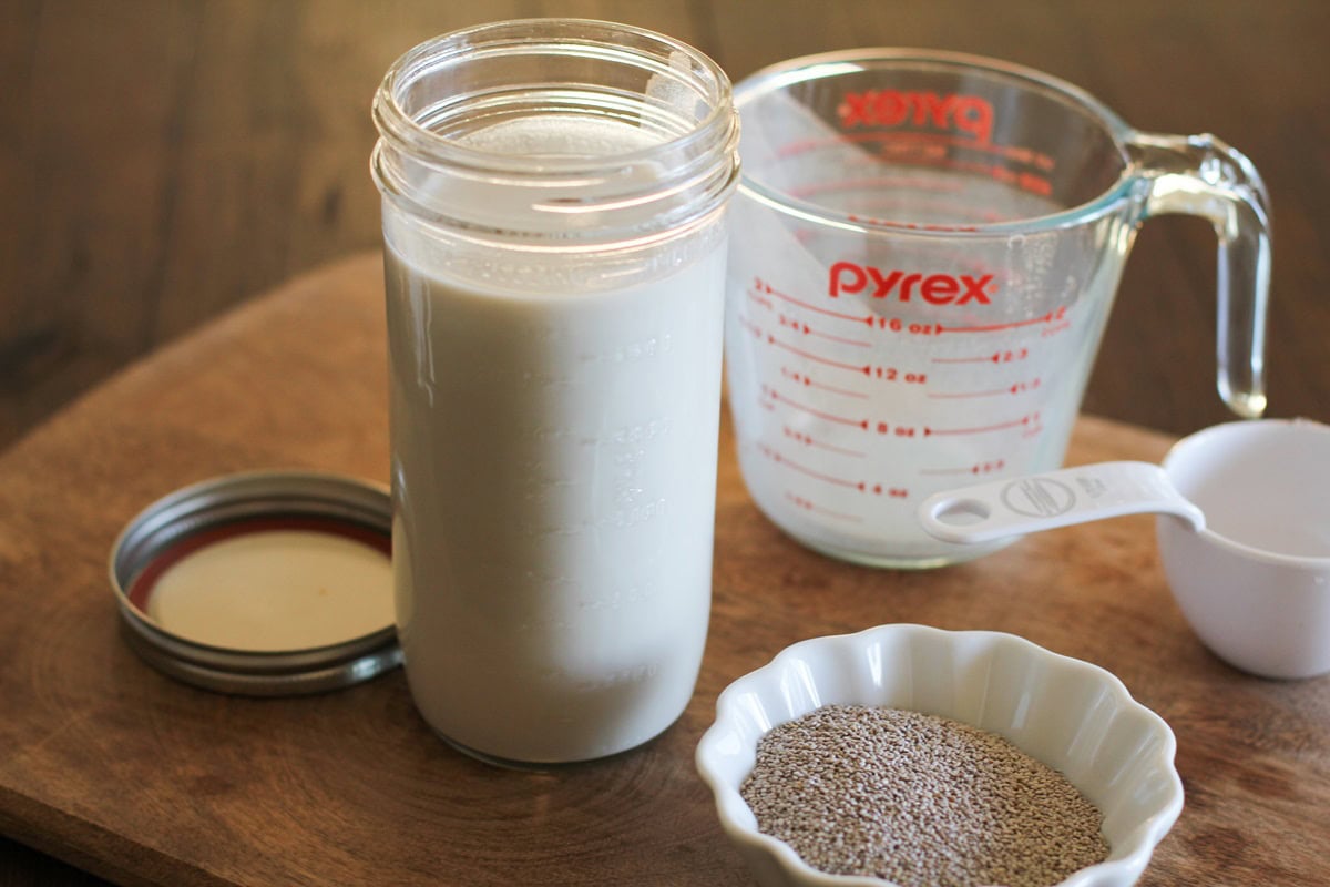 Wooden cutting board with measuring cups, a jar of milk, and a small bowl of chia seeds. Ready to turn into chia pudding.