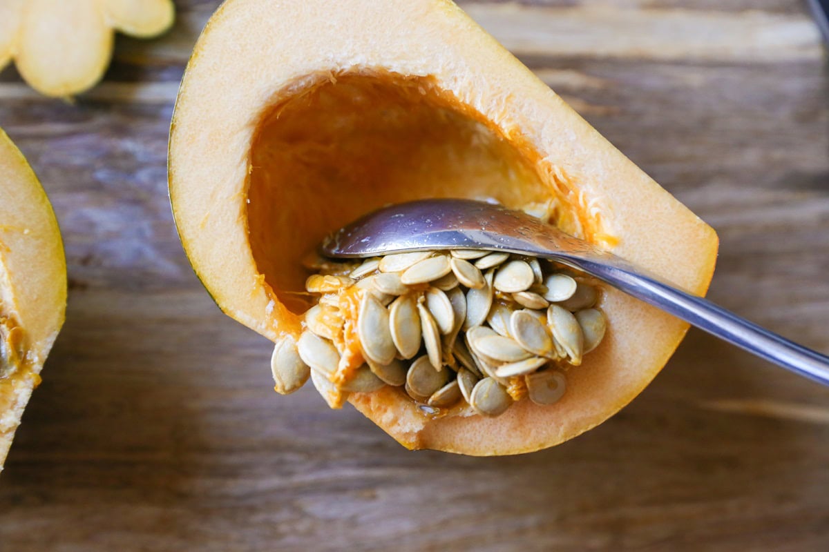 Acorn squash cut in half on a cutting board with a spoon scooping out the seeds and stringy bits.
