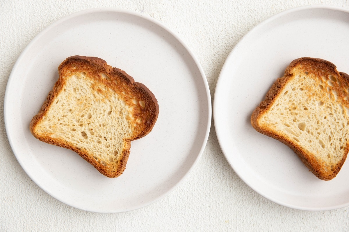 Two slices of toasted bread on two separate white plates.