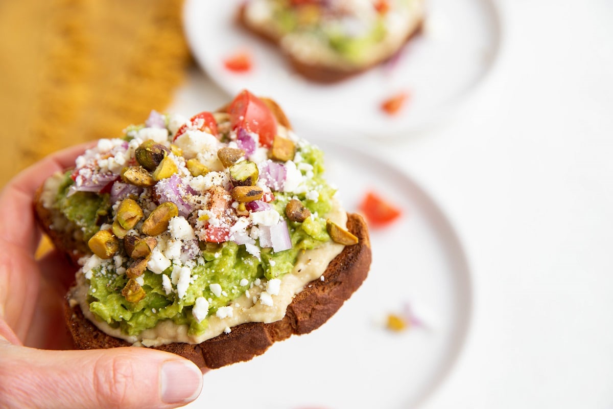 Hand holding a slice of avocado toast, ready to take a bite.