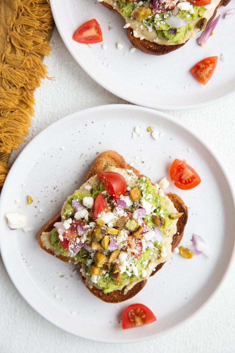 Two white plates with avocado toast slices and a golden napkin to the side.