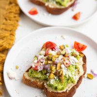 Two slices of avocado hummus toast on white plates, ready to eat.
