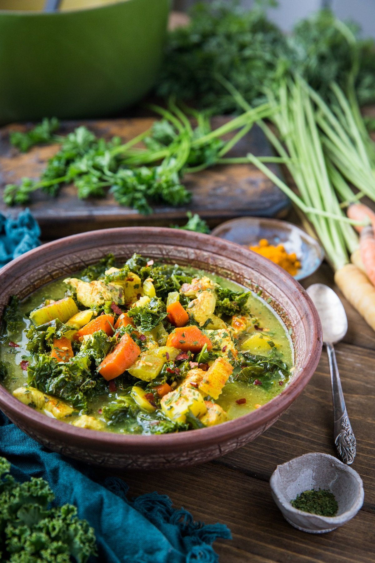 Superfood chicken soup in a bowl with carrots on rustic backdrop. Blue napkin and fresh kale leaf to the side.