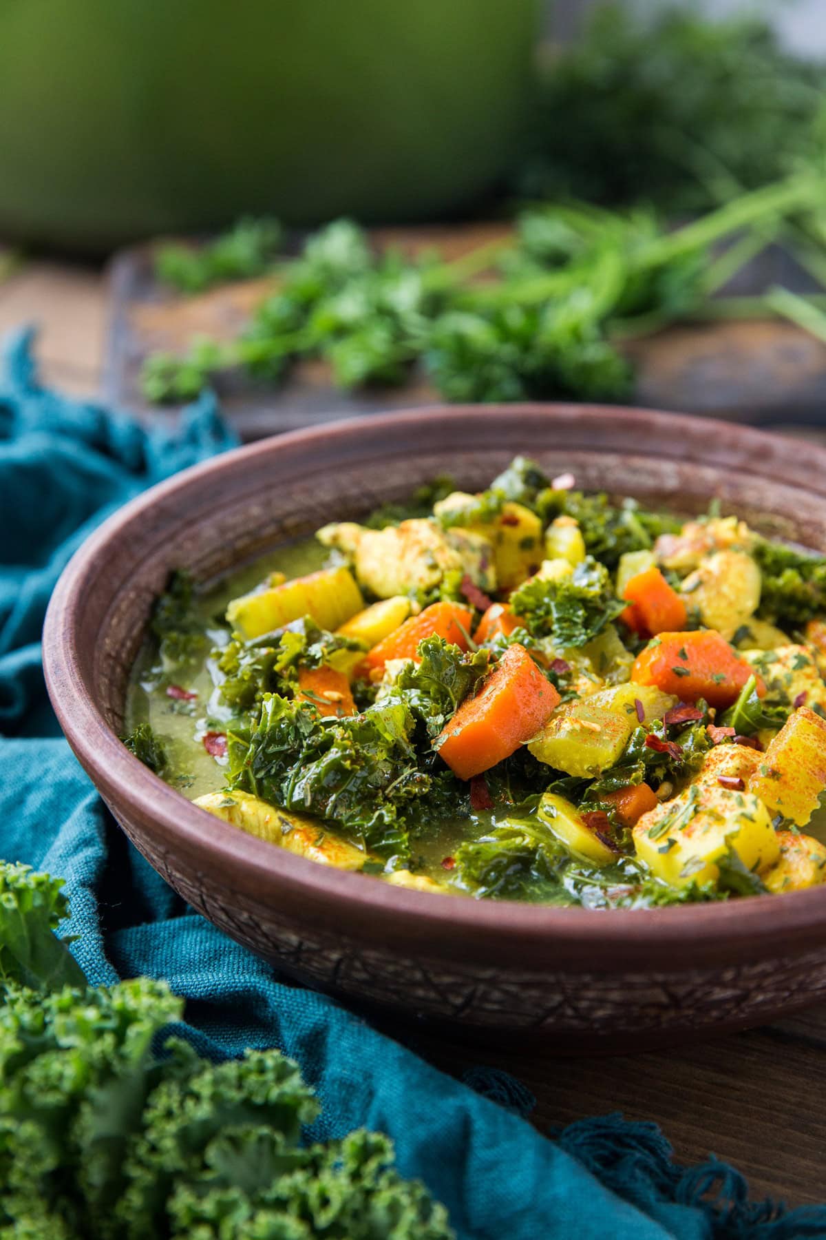 Immunity-Boosting Turmeric Chicken Soup in a bowl with a pot of soup in the background and a blue napkin to the side.