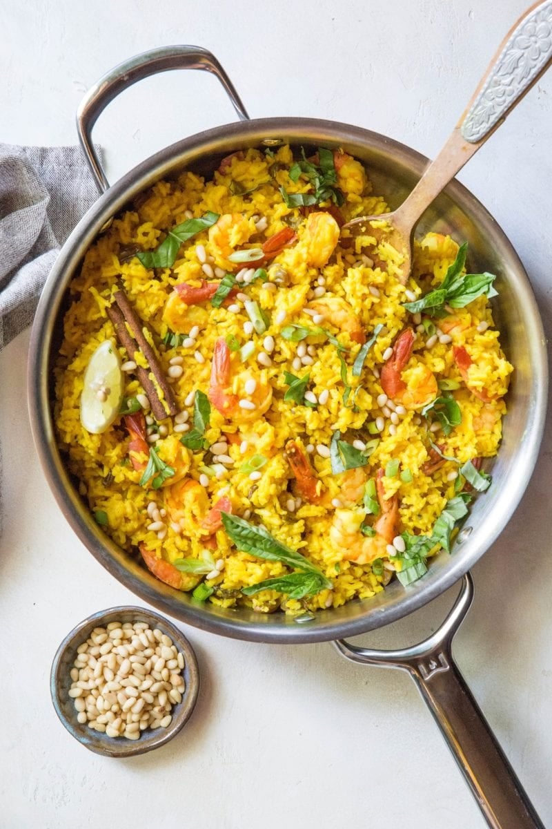 Indian Shrimp Biryani in a stainless steel skillet with a bowl of pine nuts to the side.