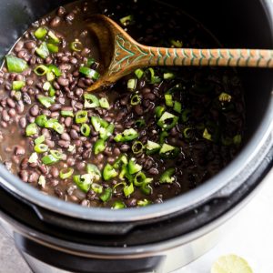 Pressure cooker full of black beans with fresh limes to the side.