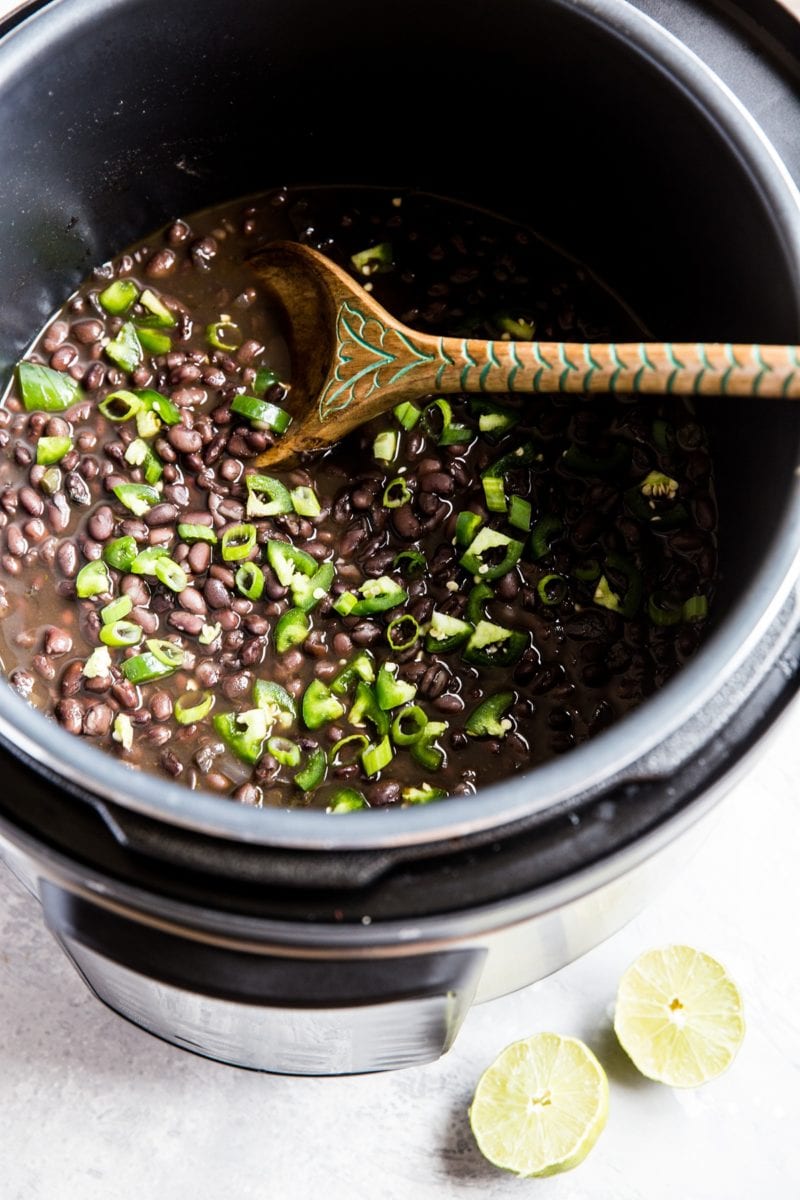 Pressure cooker full of black beans with fresh limes to the side.