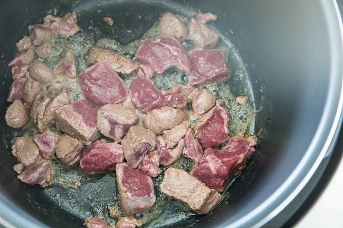 Chunks of lamb cooking in an Instant pot, browning to make lamb curry.