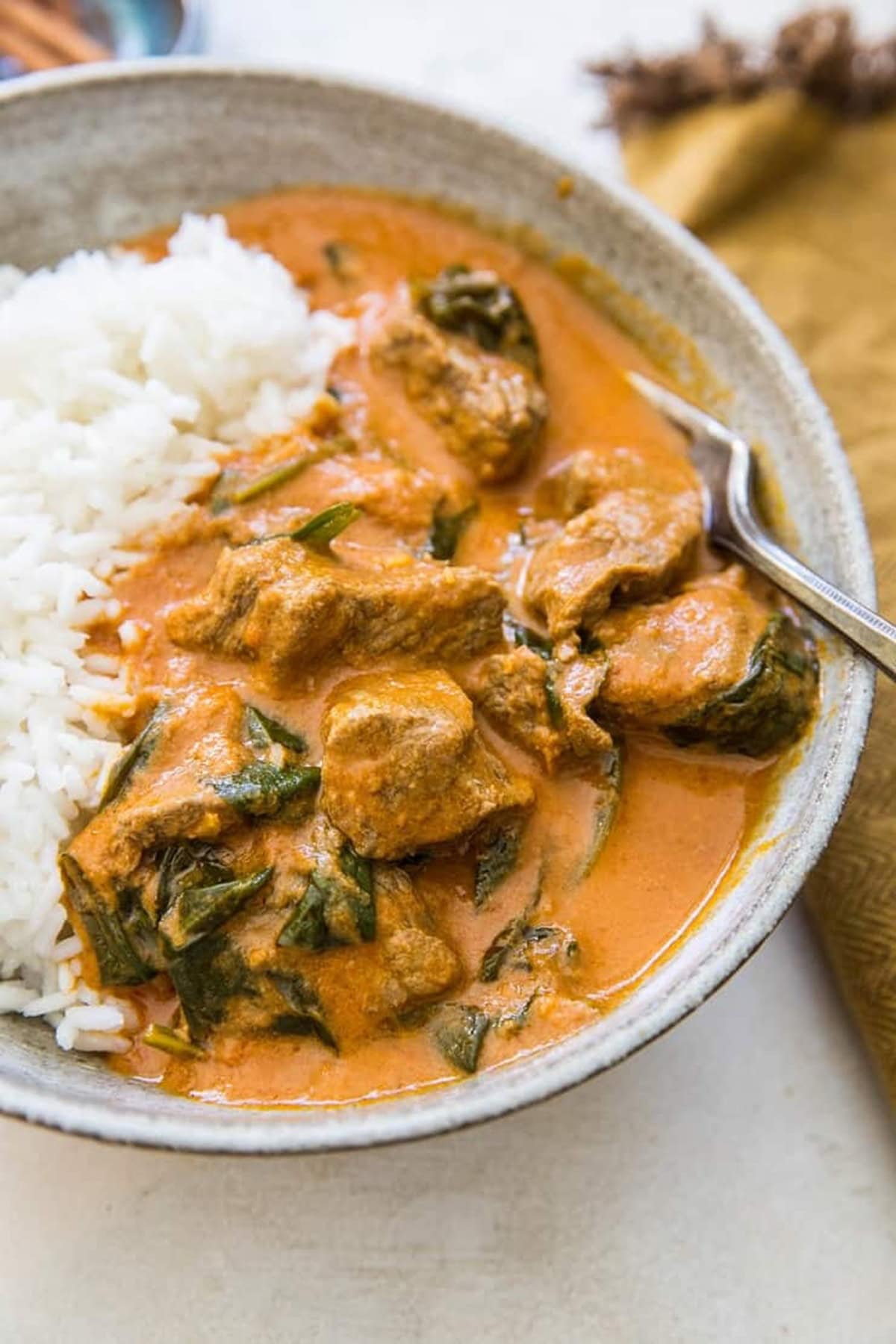 Large bowl of rice and Indian lamb curry with a fork to the side and a golden napkin in the background.