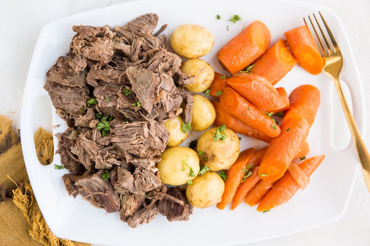Shredded beef, gold potatoes, and chunks of carrots on a white platter with a serving fork. Ready to serve.