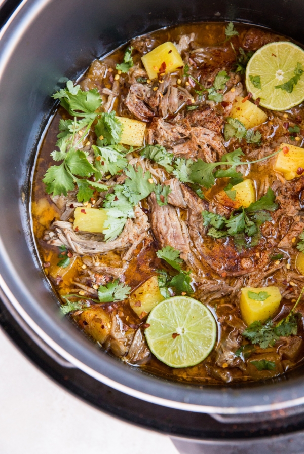 Instant pot full of shredded pork in juices with chunks of pineapple and a sprinkle of red pepper flakes and fresh cilantro. Ready to serve as a main dish.