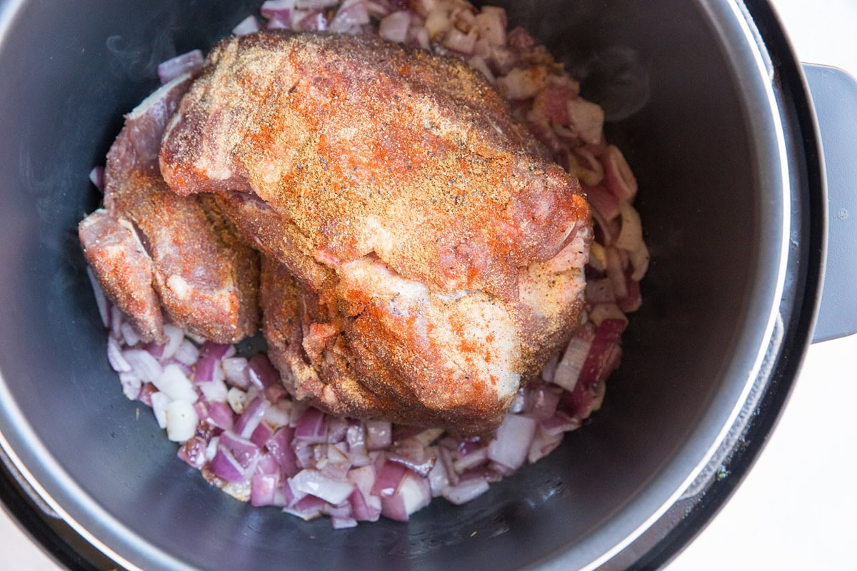 Seasoned pork roast browning in a pressure cooker with onions.