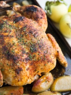 Whole juicy chicken sitting on a large baking sheet with cooked apples all around. Ready to serve with side dishes.