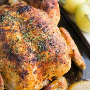 Whole juicy chicken sitting on a large baking sheet with cooked apples all around. Ready to serve with side dishes.