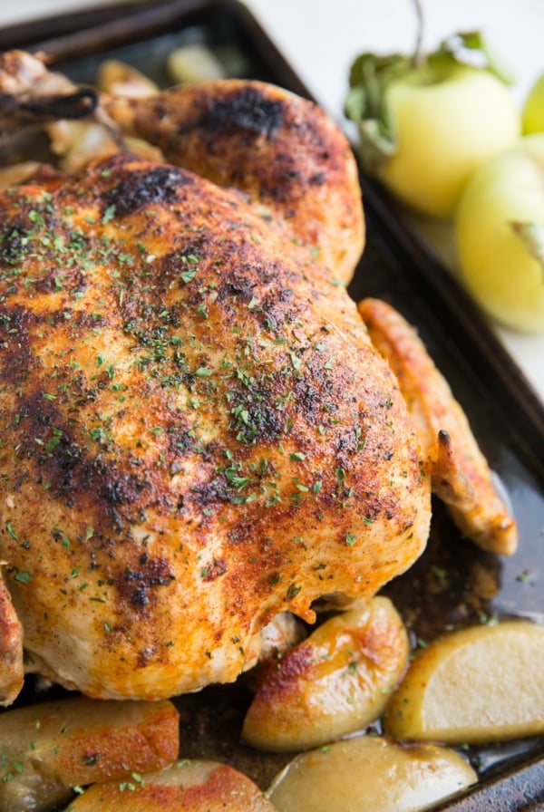 Whole juicy chicken sitting on a large baking sheet with cooked apples all around. Ready to serve with side dishes.