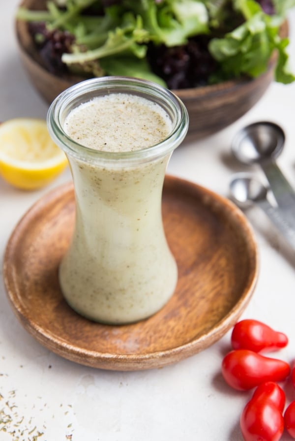 Italian salad dressing in a glass container with fresh tomatoes to the side and a salad in the background.