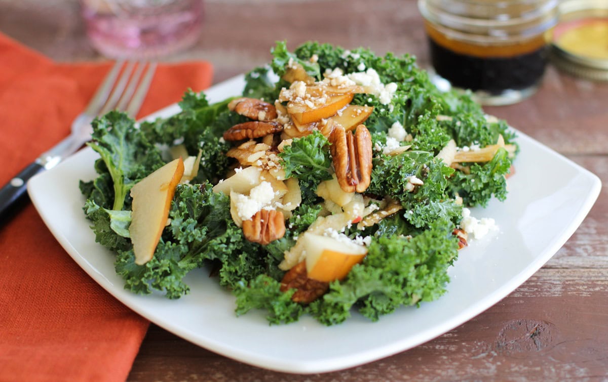 kale salad with pears and pecans on a plate with balsamic vinaigrette, ready to serve.