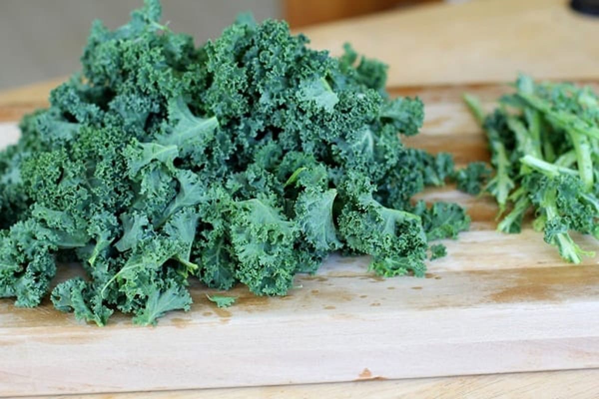 kale leaves on a cutting board with the stems to the side.