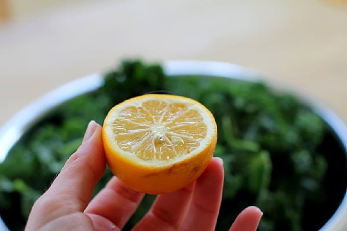 Hand holding a half of a lemon above a bowl of chopped kale, ready to squeeze the lemon juice over the kale.