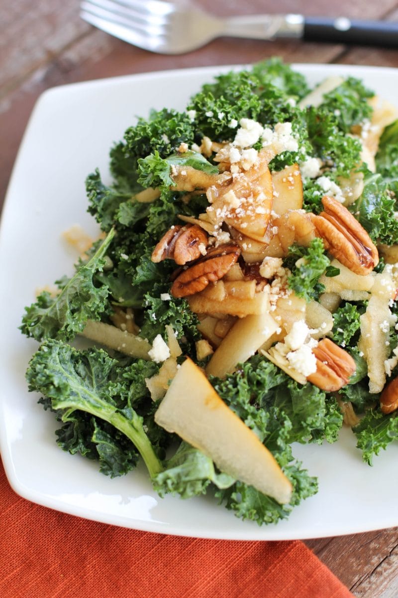 Massaged Kale Salad with Apple, Pear, Gorgonzola and Roasted Pecans on a white plate with a red napkin to the side.