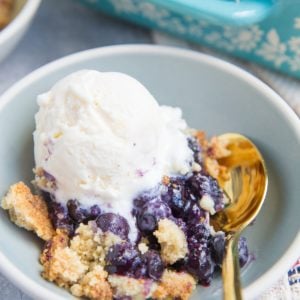 Keto Blueberry Cobbler in a bowl with a scoop of vanilla ice cream and a gold spoon to the side.