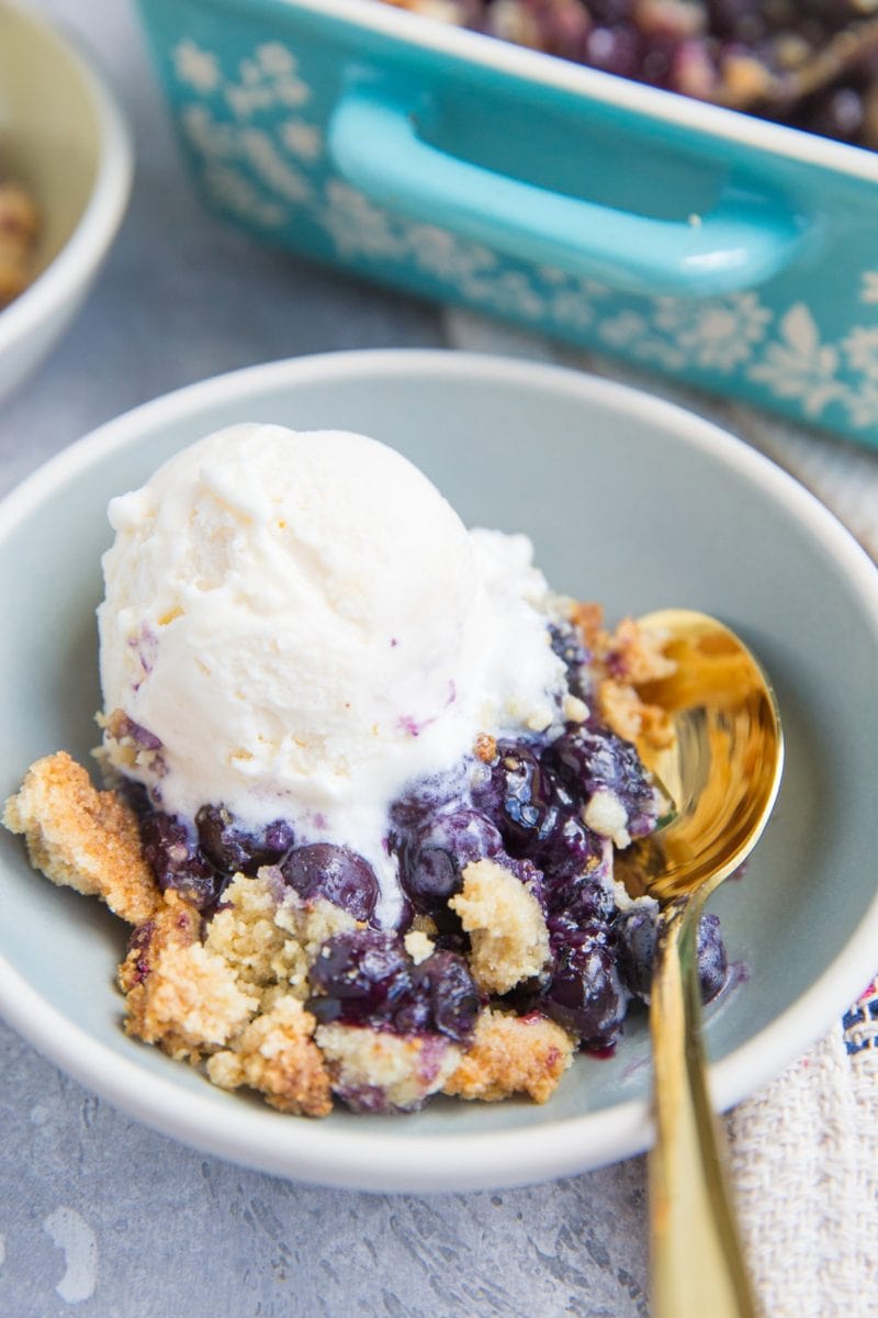 Keto Blueberry Cobbler in a bowl with a scoop of vanilla ice cream and a gold spoon to the side.