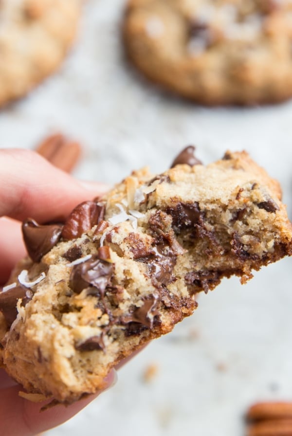 Hand holding a large keto cowboy cookie with a bite taken out, exposing the soft center. Soft, chewy, gooey keto cowboy cookies.