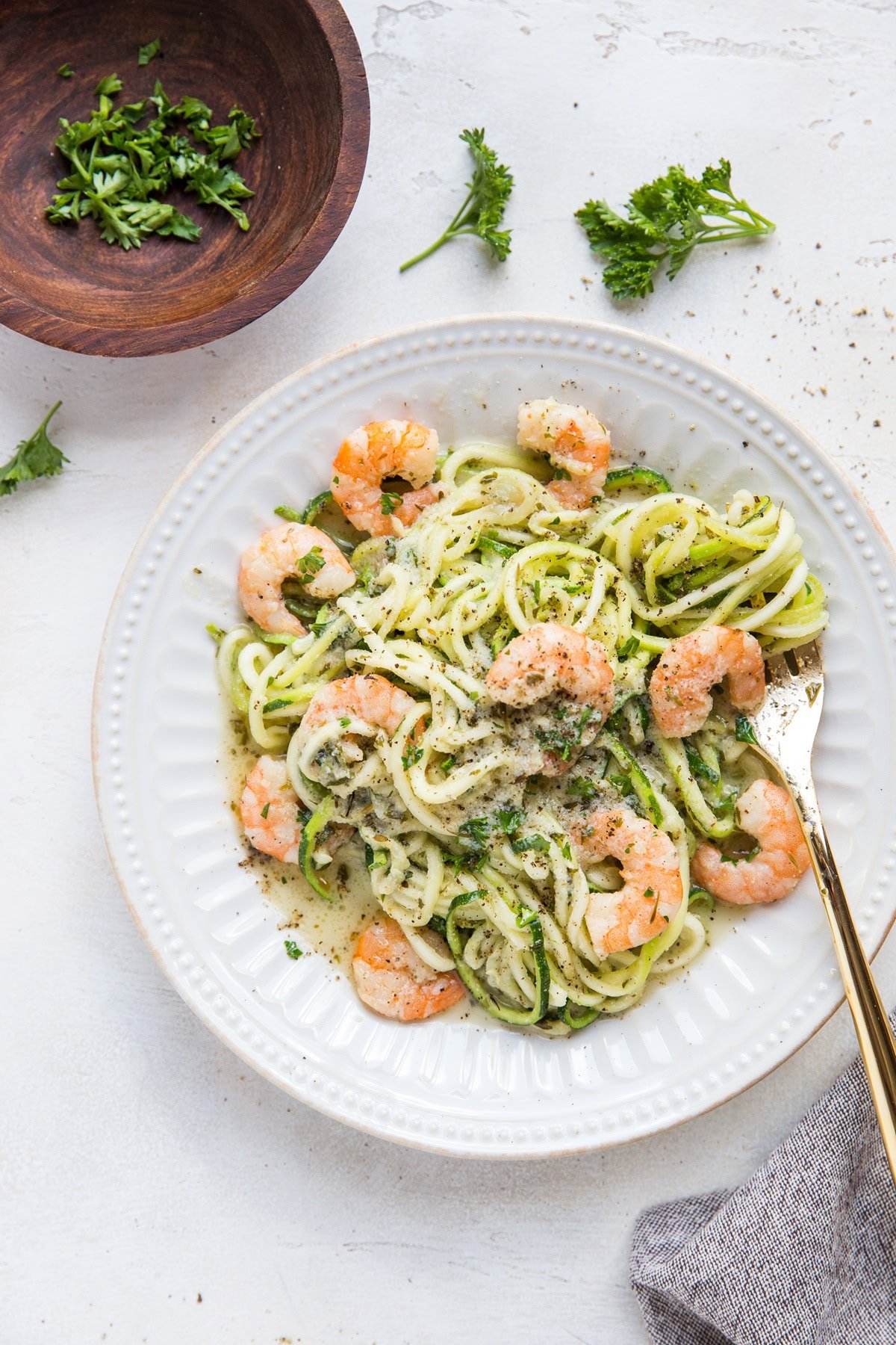 Zucchini noodles and shrimp on a white plate with a golden fork, ready to eat.