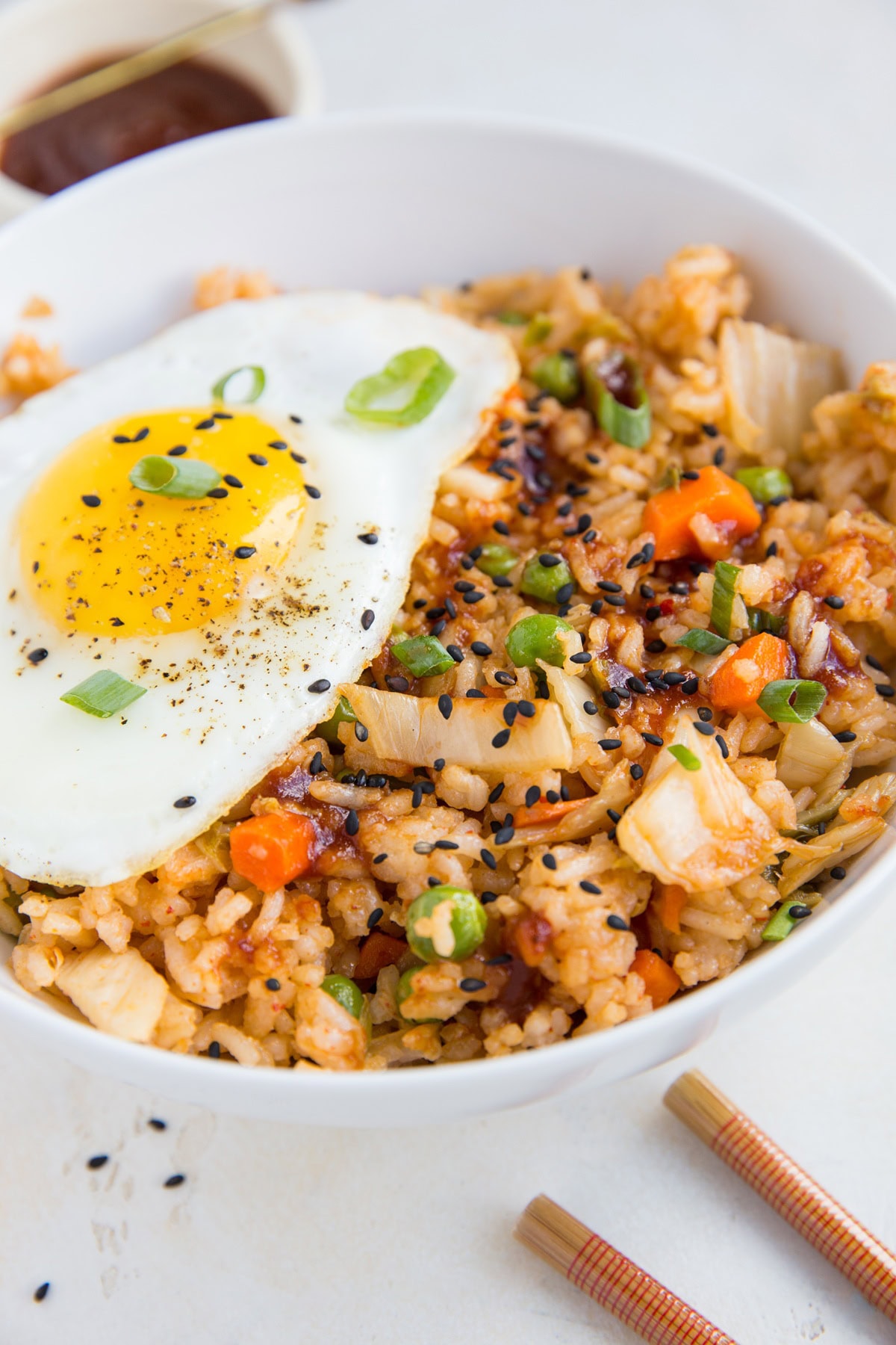 Kimchi Fried Rice in a large white bowl with a fried egg on top and chop sticks to the side.