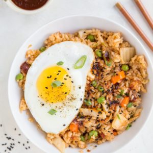 Large white bowl full of kimchi fried rice with a fried egg on top and sprinkles of sesame seeds to the side.