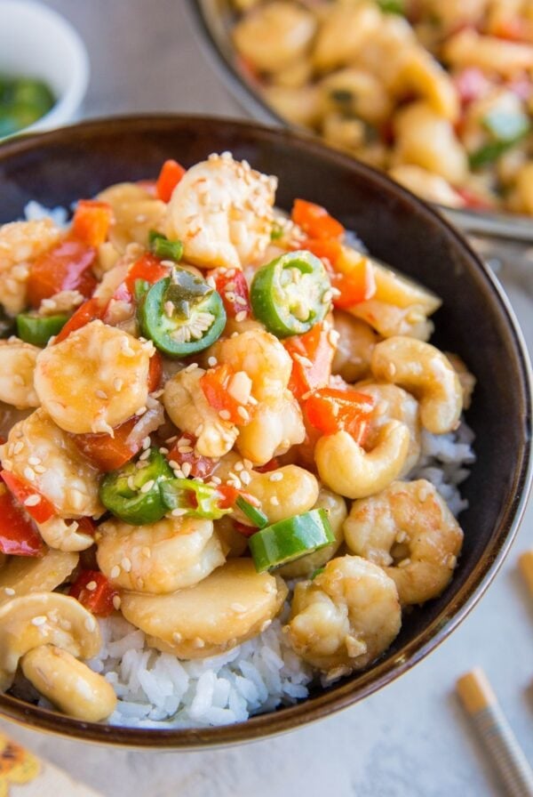 Large ceramic bowl full of kung pao shrimp on top of white rice with chop sticks to the side.