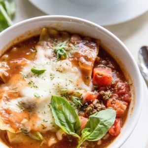Instant Pot Lasagna Soup in a white bowl with melted mozzarella and fresh basil on top.