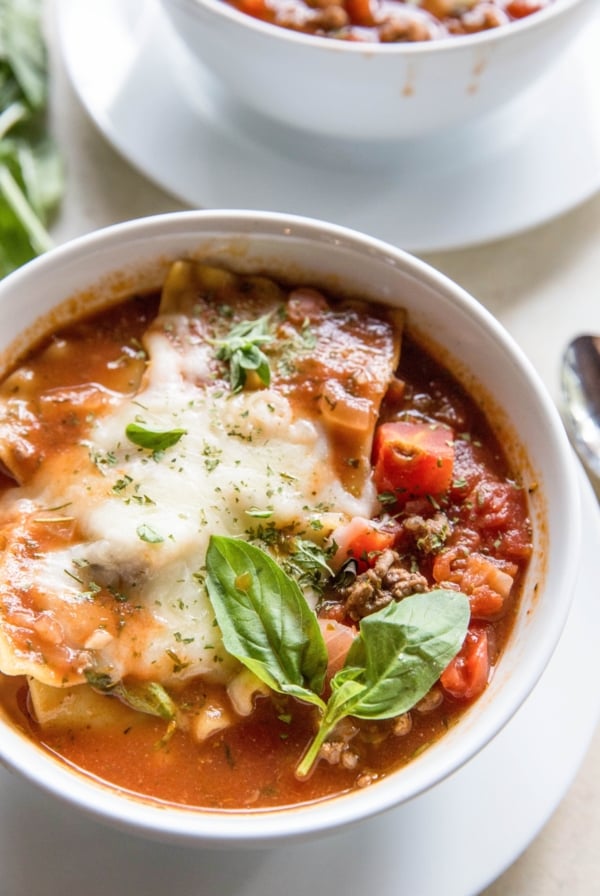 Instant Pot Lasagna Soup in a white bowl with melted mozzarella and fresh basil on top.