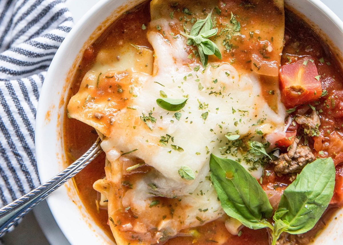 large white bowl of lasagna soup with melted cheese on top and a silver spoon digging in.