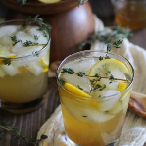 Two lemon thyme bourbon cocktails on a wooden background with fresh thyme and lemon wedges.