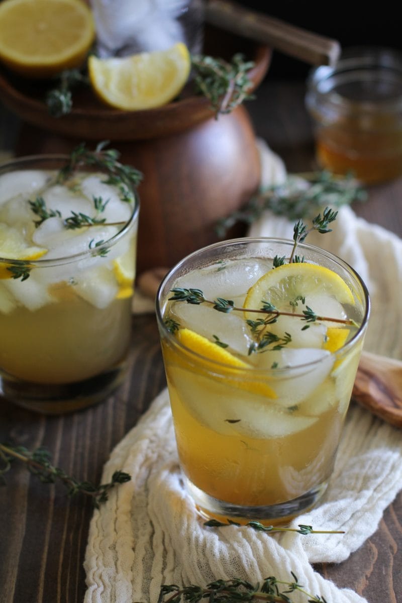Two lemon thyme bourbon cocktails on a wooden background with fresh thyme and lemon wedges.
