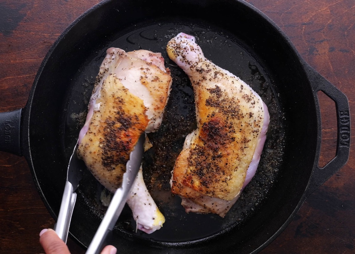 Skin on chicken legs being seared in a cast iron skillet with golden brown skin.
