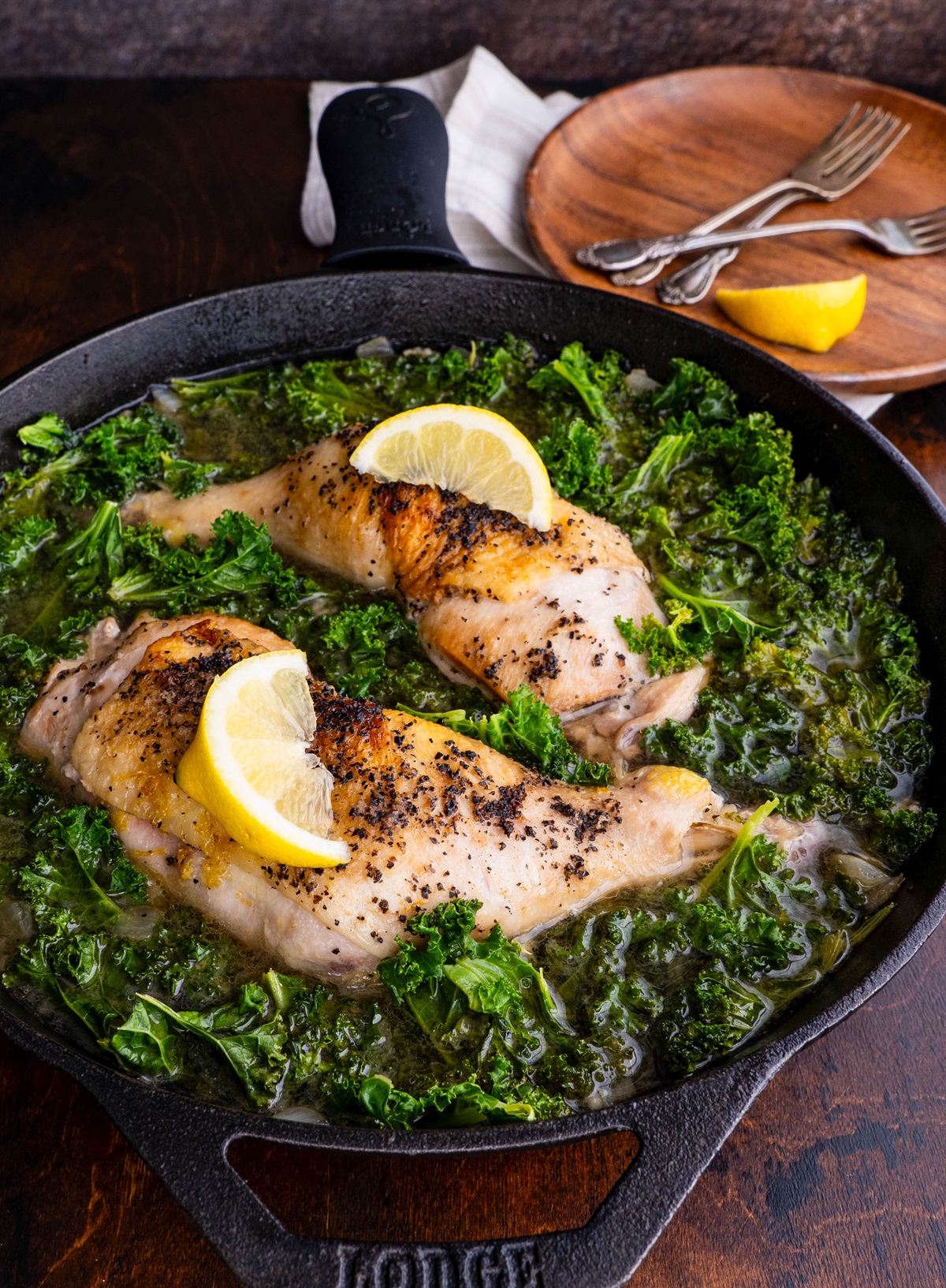 Chicken pieces in a cast iron skillet with braised kale. Ready to eat.