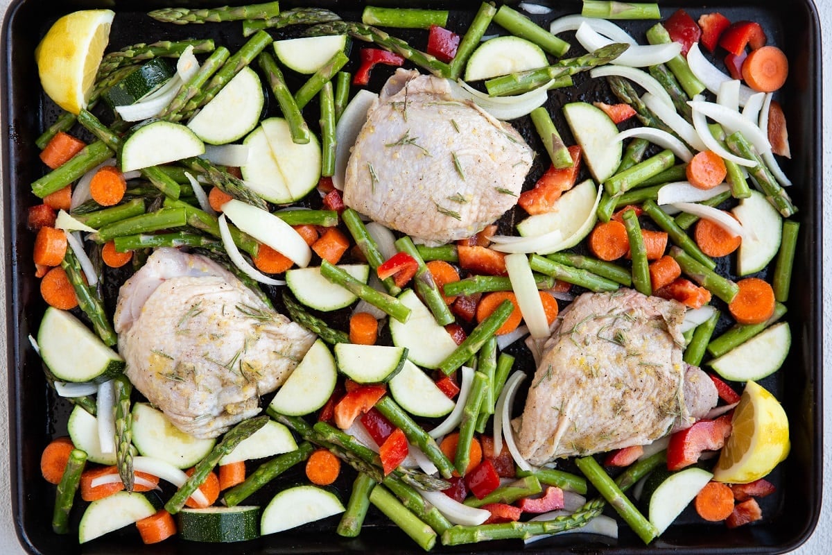 Raw chicken thighs and vegetables on a sheet pan, ready to go into the oven.