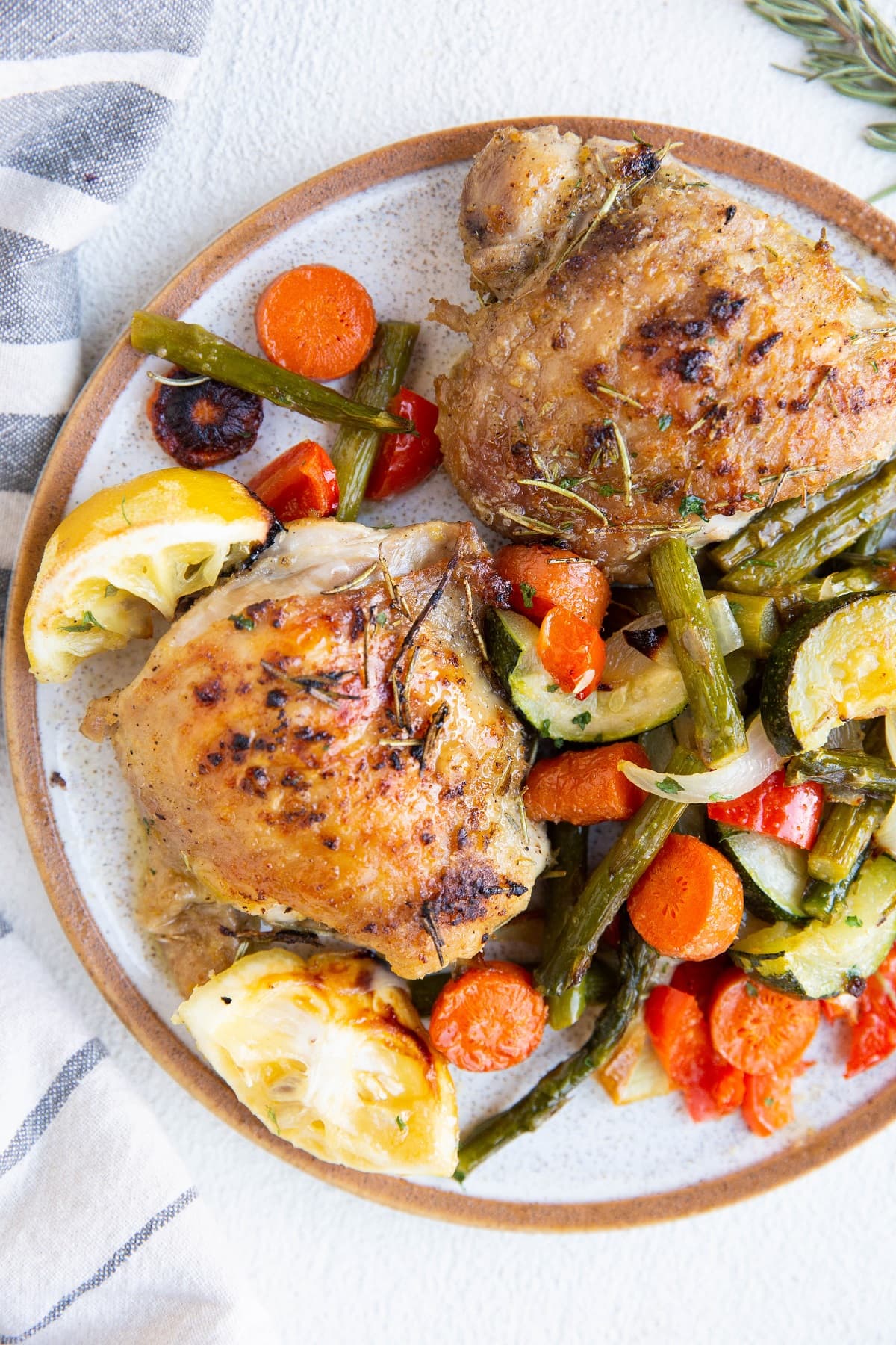 Plate with chicken thighs and roasted vegetables on it, ready to eat.