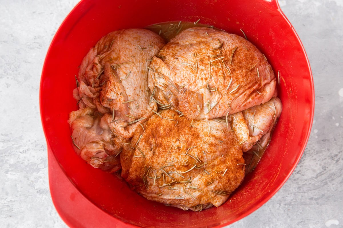 Chicken thighs in seasonings and marinade in a large bowl.