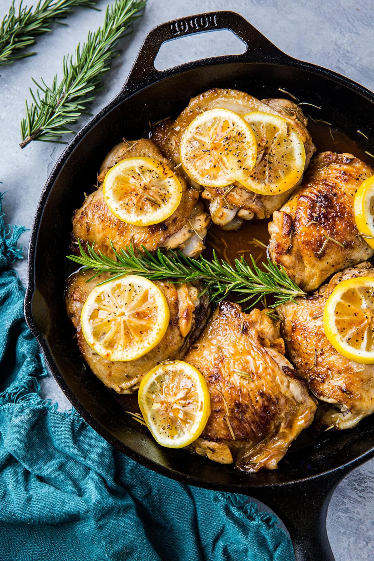 Lemon rosemary braised chicken thighs in a cast iron skillet, ready to serve. A blue napkin to the side.