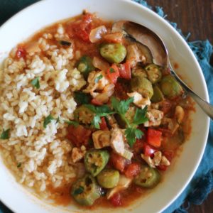 Louisiana-Style Chicken Soup with Okra in a large white bowl with brown rice to the side and a blue napkin, ready to eat