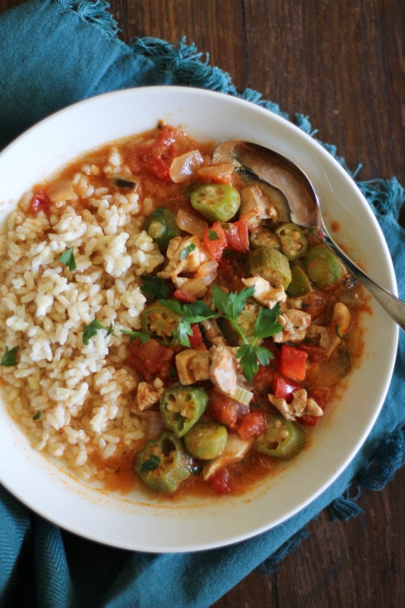 Louisiana-Style Chicken Soup with Okra in a large white bowl with brown rice to the side and a blue napkin, ready to eat
