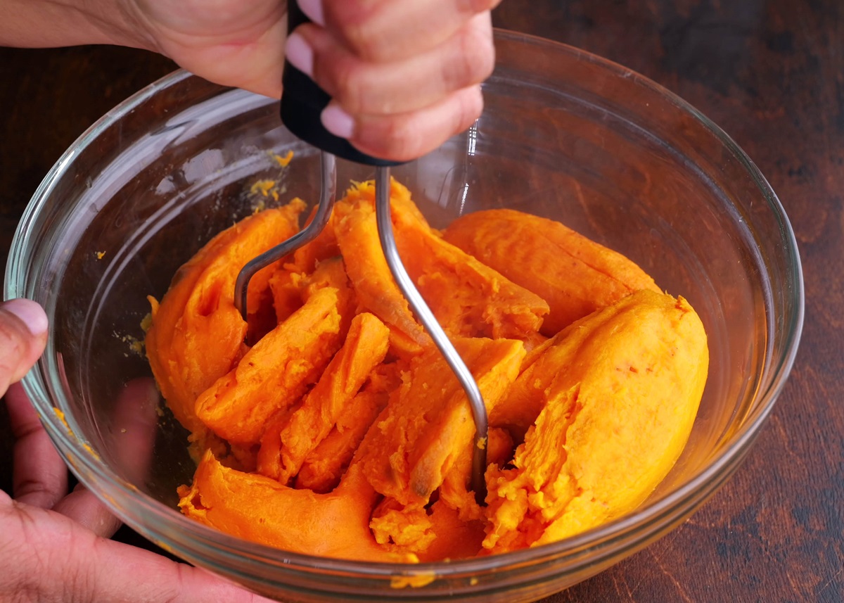 Mashing sweet potatoes with a potato masher in a mixing bowl.