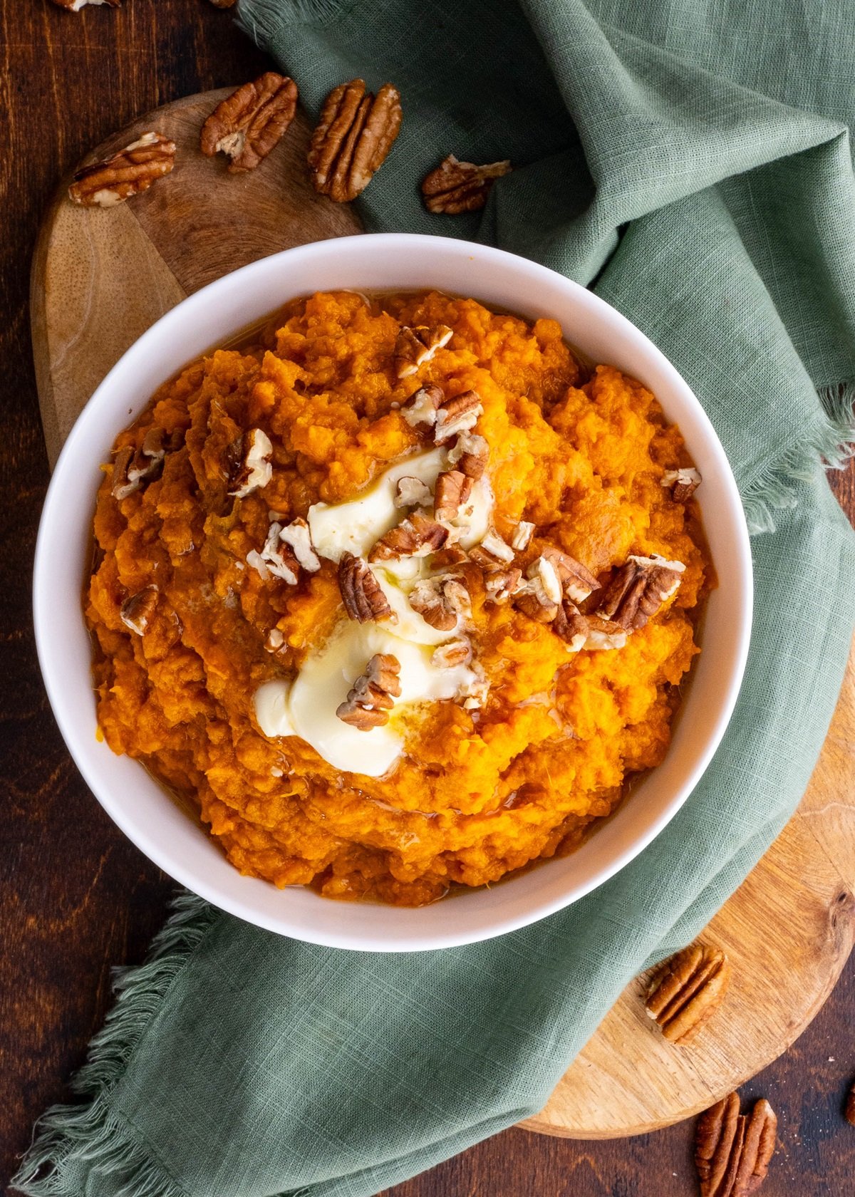 White bowl of mashed sweet potatoes with melted butter and chopped pecans on top.