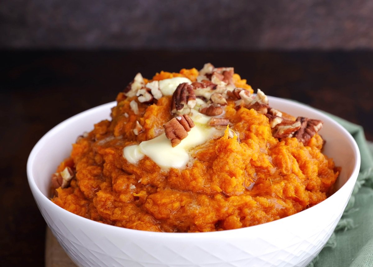 Maple-Bourbon Mashed Sweet Potatoes in a white bowl with melted butter and pecans on top.