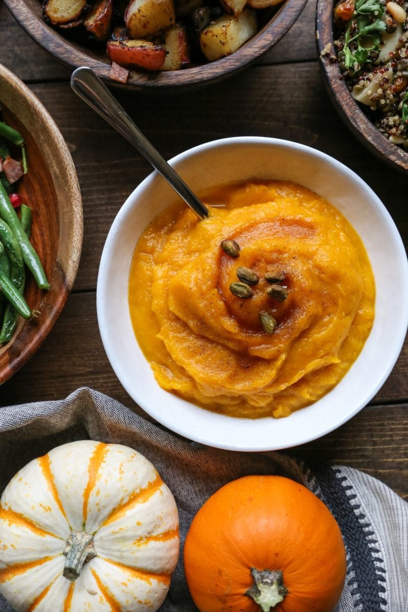 Bowl of kabocha squash mash with other side dishes all around.